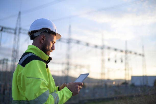 Worker using tablet standing in a field near a substation